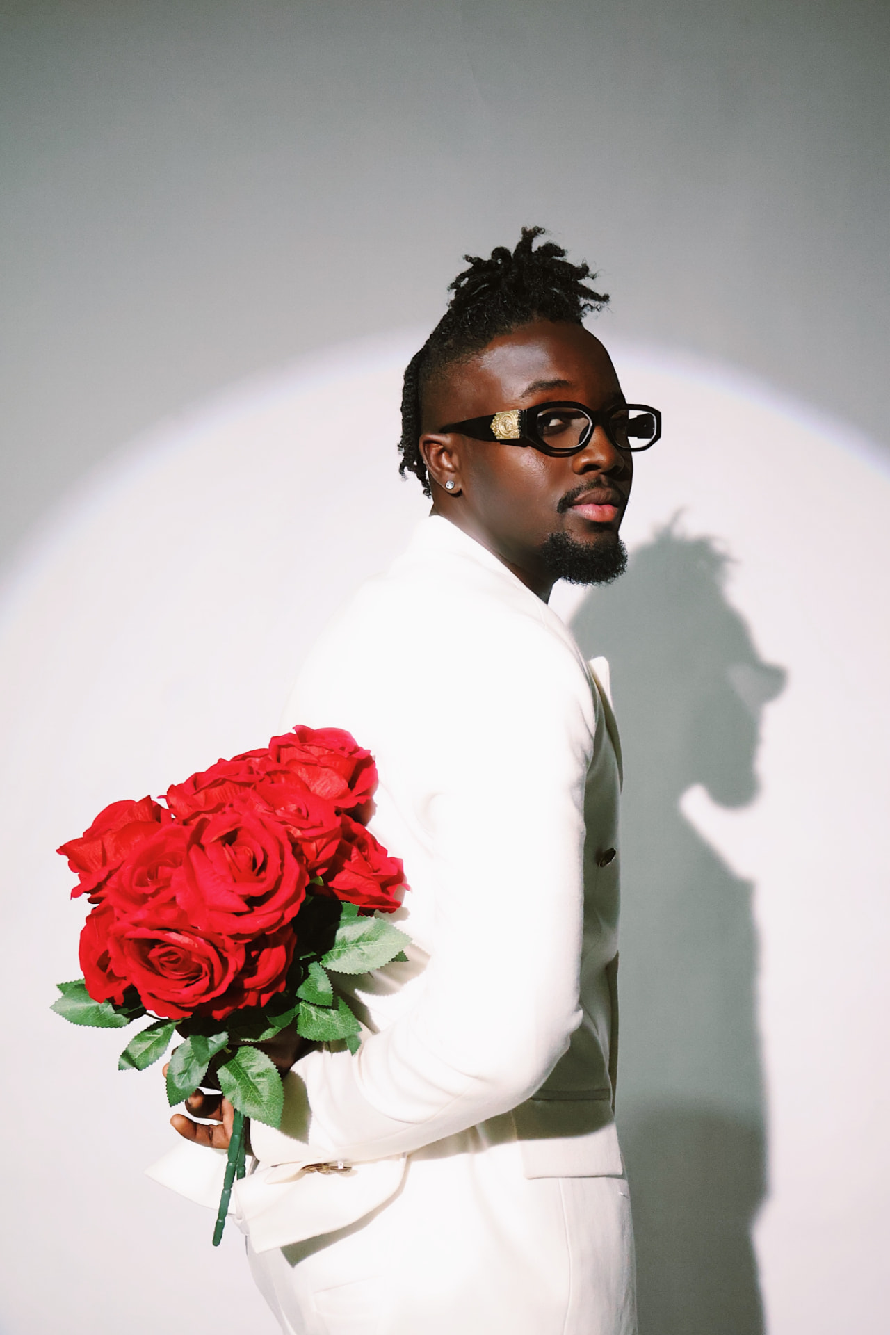 Broni in a cream suit holding a bouquet of red roses